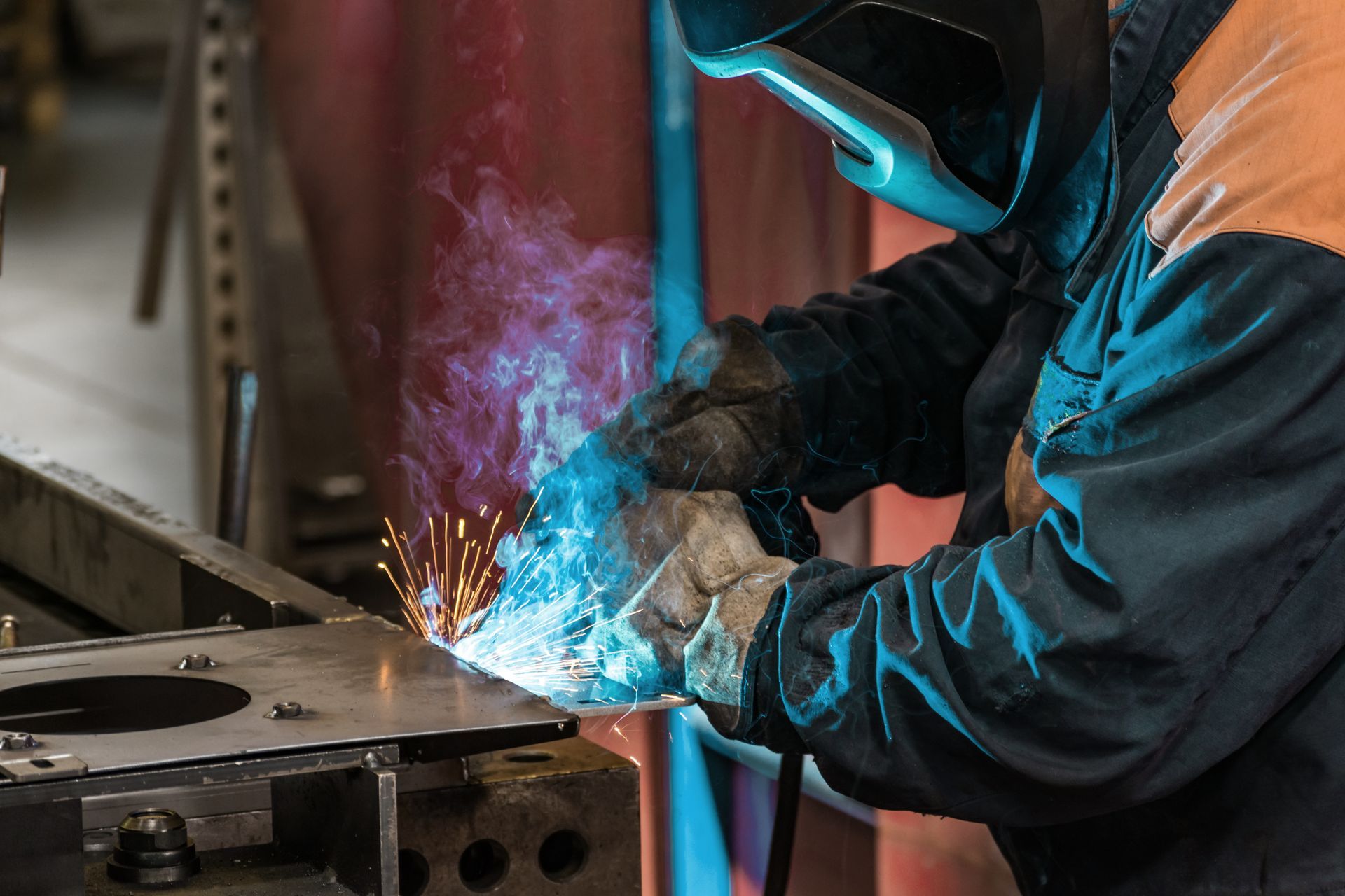 Welder in protective gear welding metal, sparks and bright blue light.