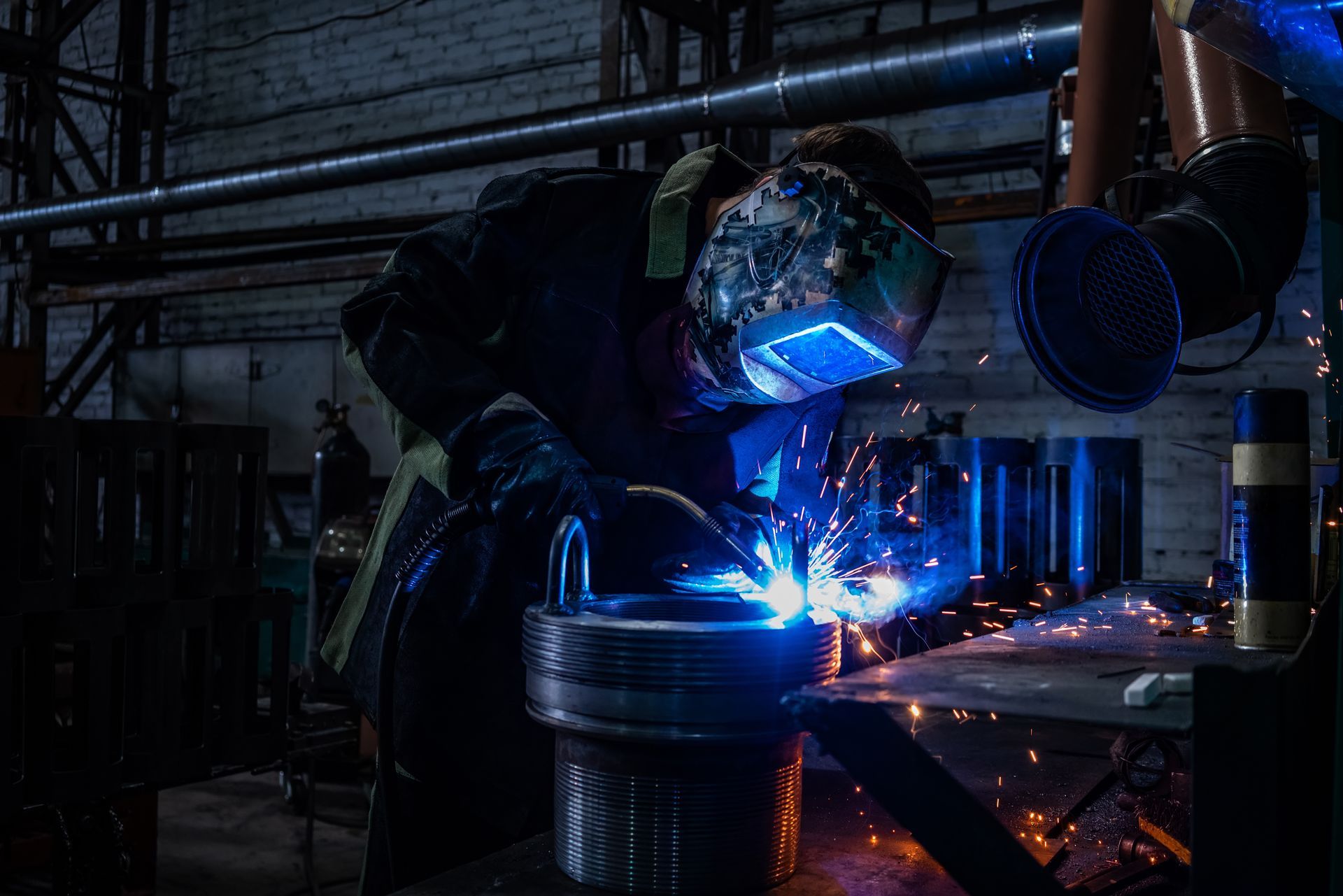 Welder in dark workshop, sparks flying, welding metal with a bright blue light from the mask.