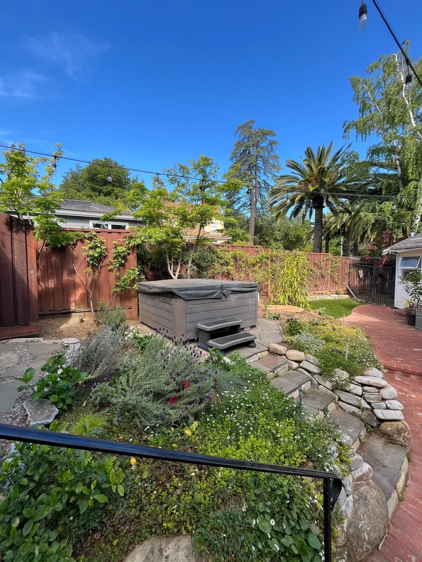 Backyard with hot tub, garden, and a clear blue sky.