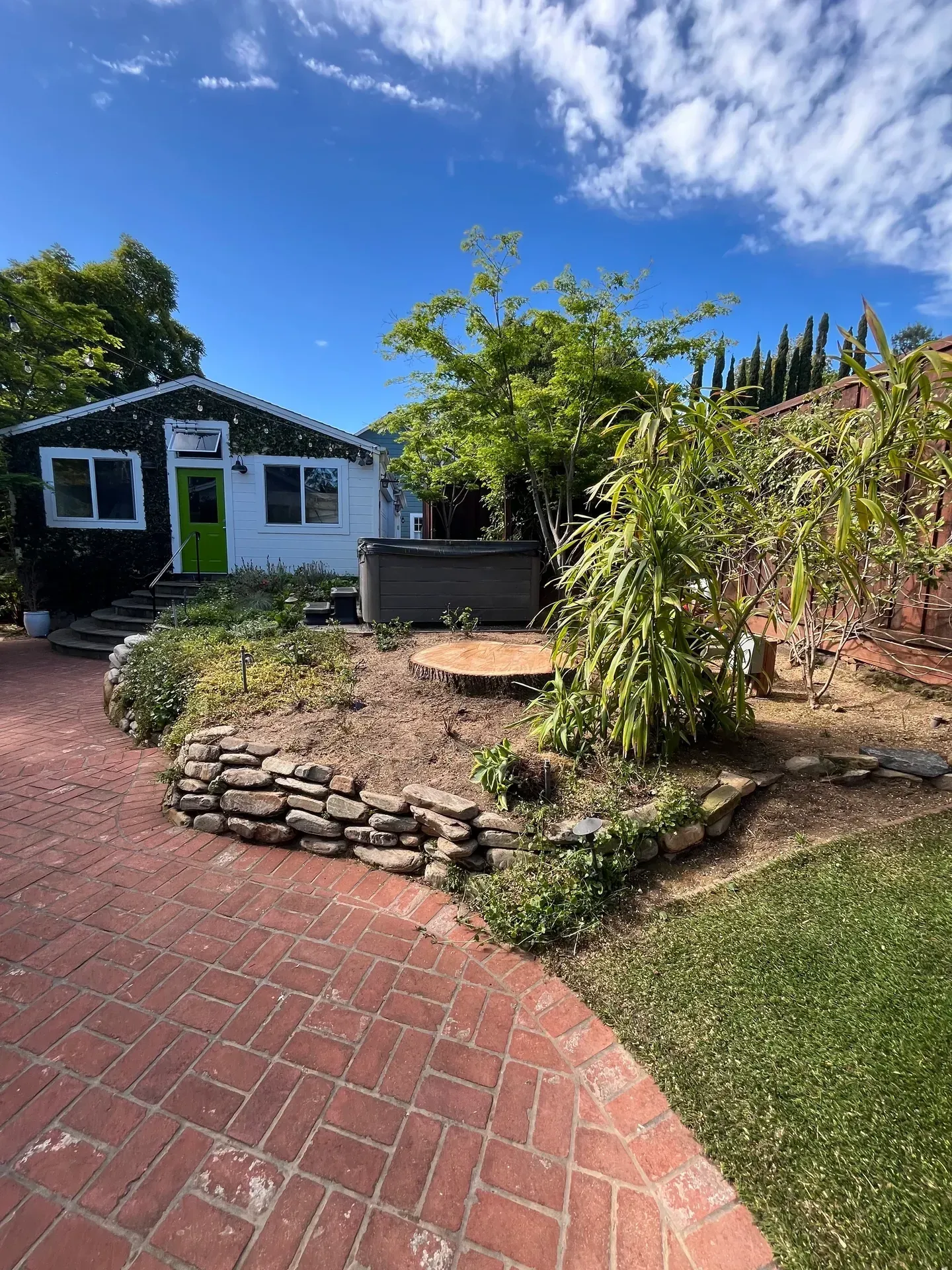 A small white house with a green door, a brick pathway, and a garden under a blue sky.