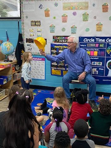 A man is sitting in front of a group of children in a classroom.