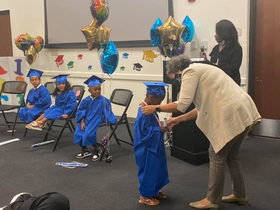 A woman is helping a young boy in a graduation cap and gown.