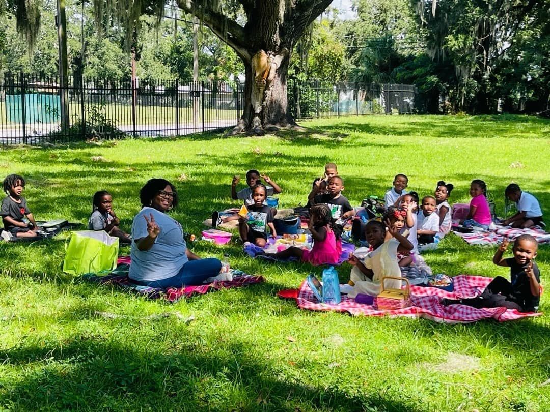 A group of children are sitting on blankets in the grass in a park.