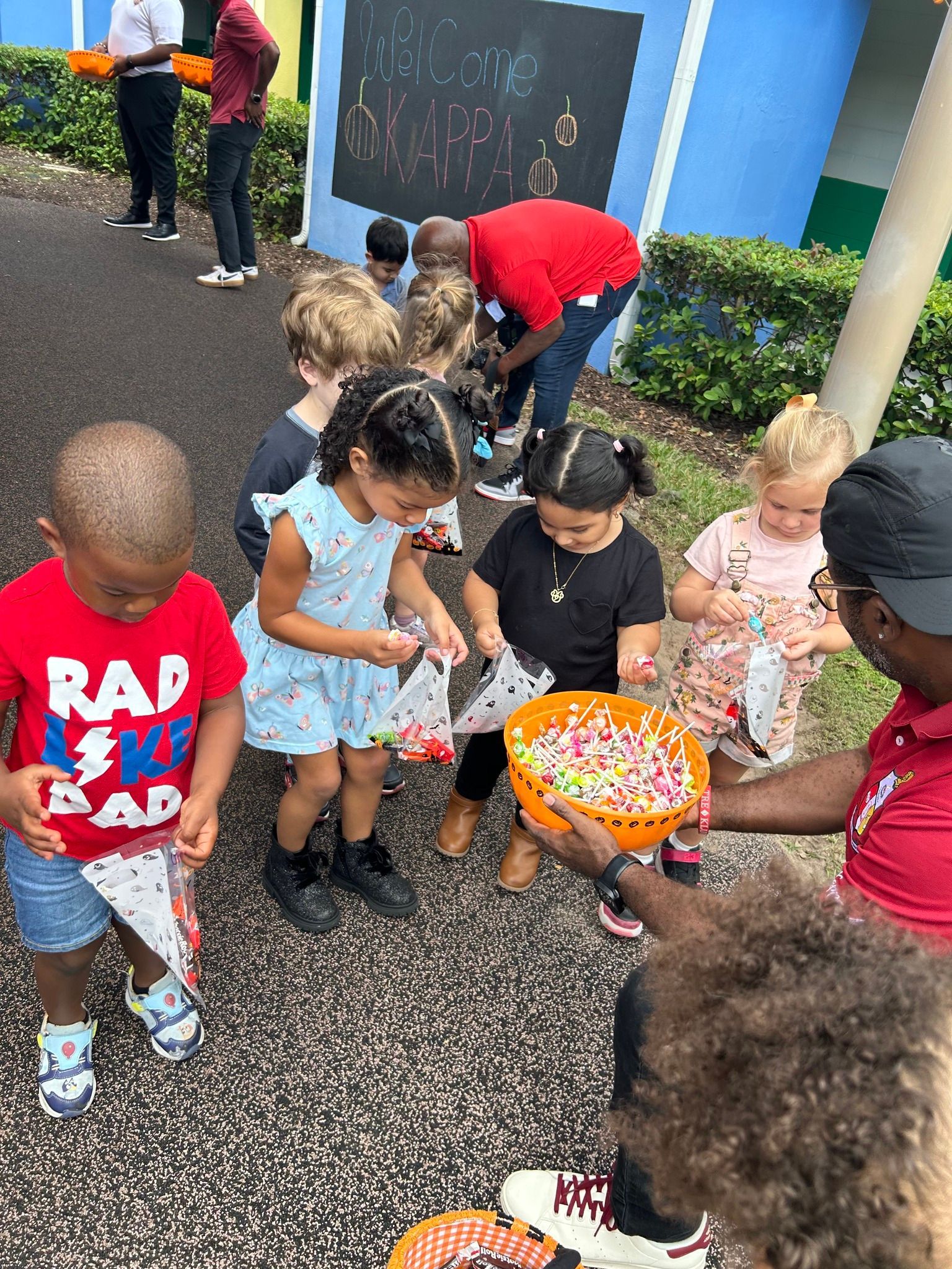 A group of children are standing around a man holding a basket of candy.