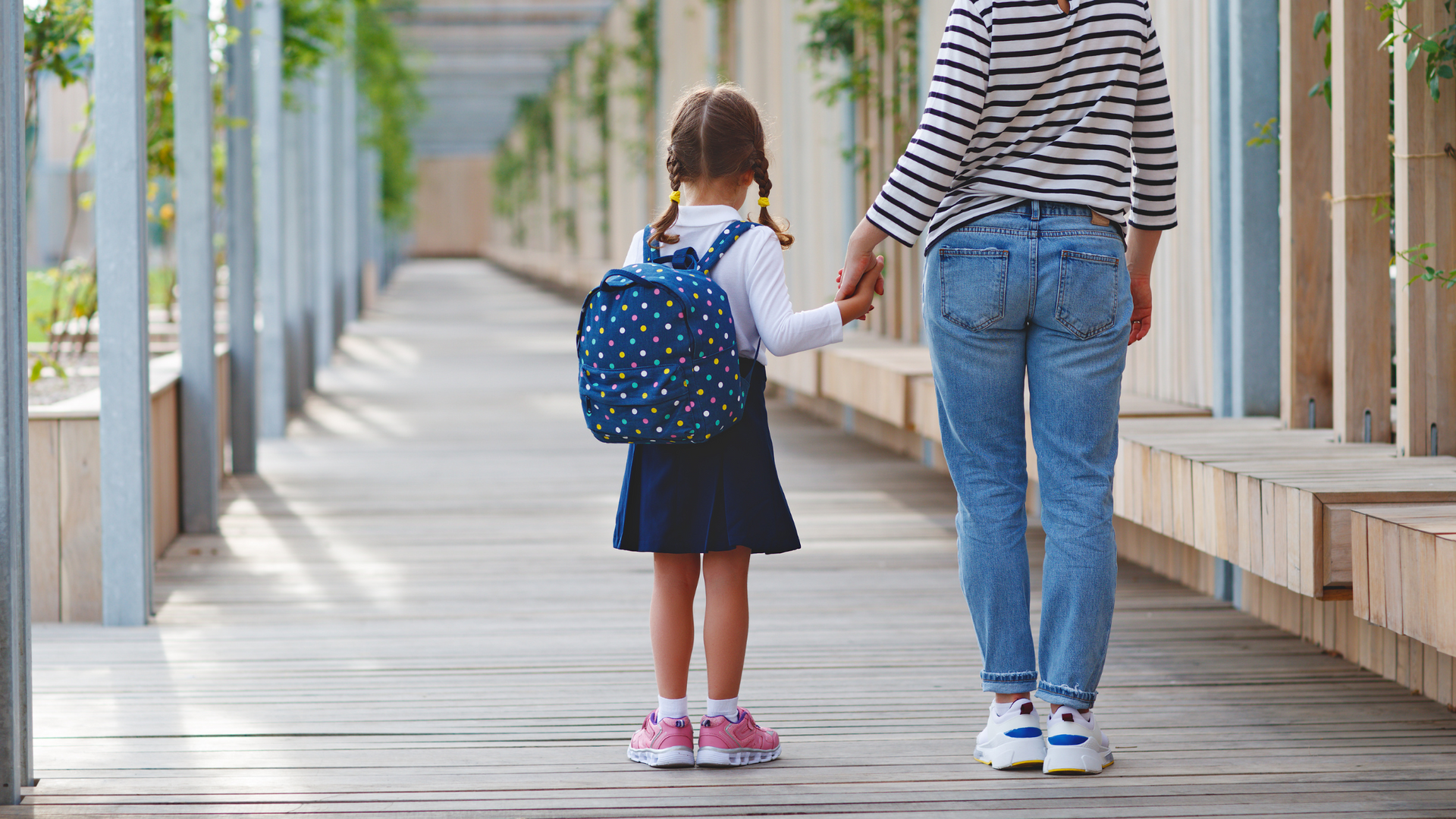 A woman is holding a little girl 's hand while walking down a wooden walkway.