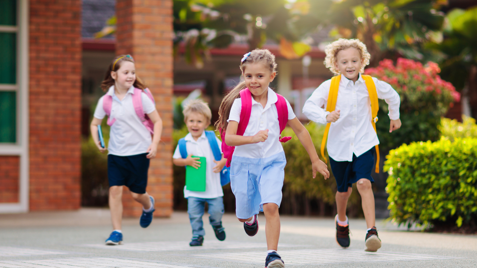 A group of children with backpacks are running towards a school building.