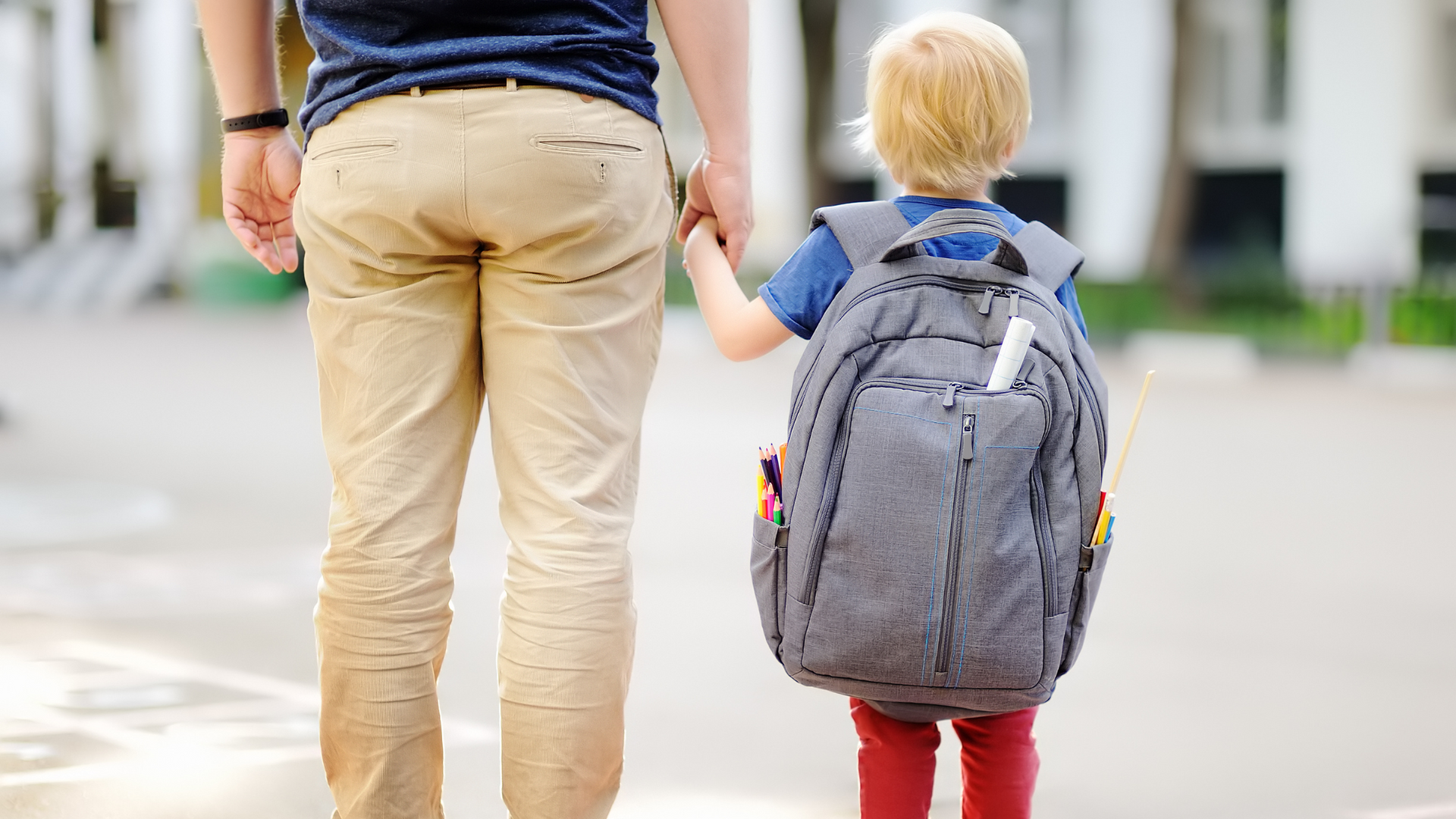 A man is holding the hand of a little boy with a backpack.