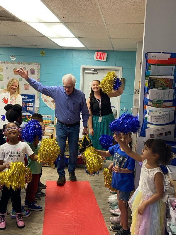 A man is walking down a red carpet with children holding pom poms.