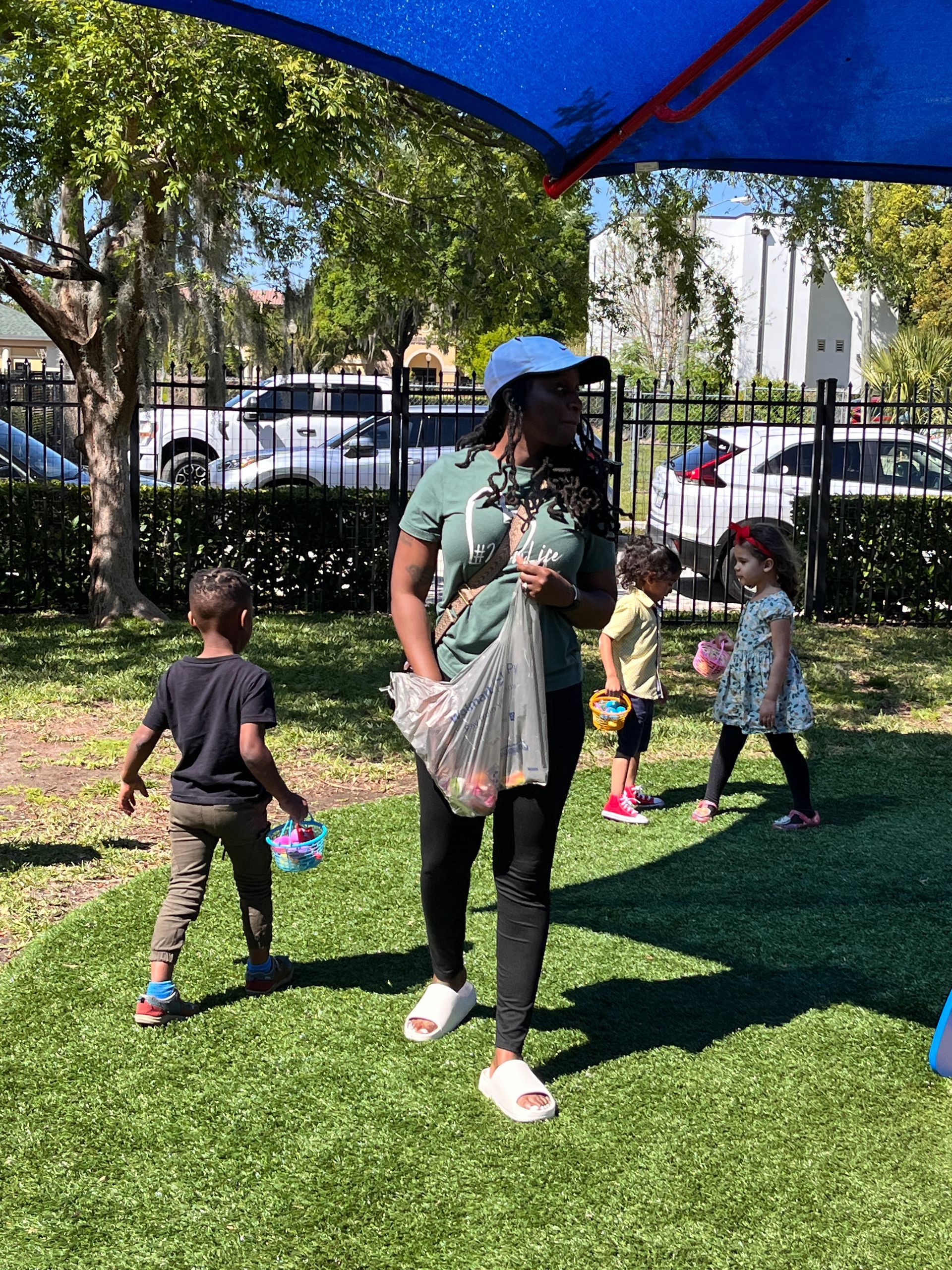 A woman is standing in the grass with children under an umbrella.