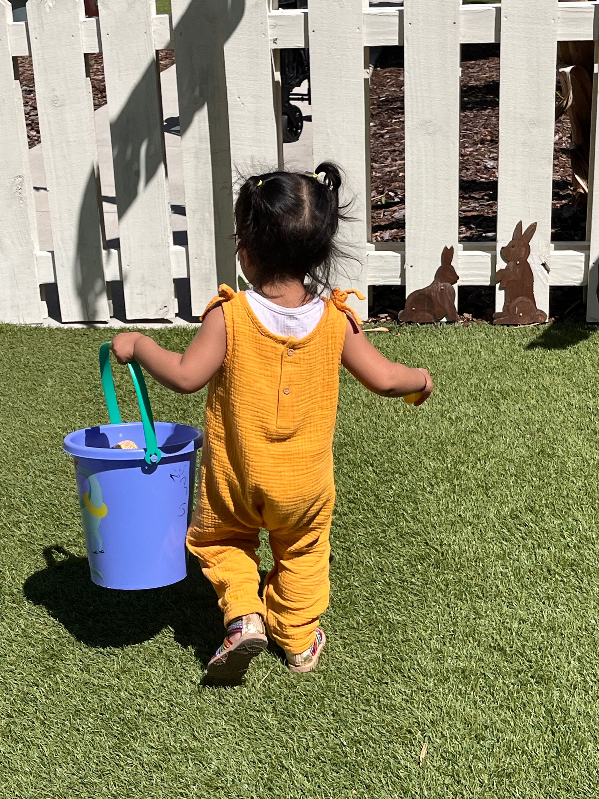 A little girl is walking with a blue bucket in her hand.