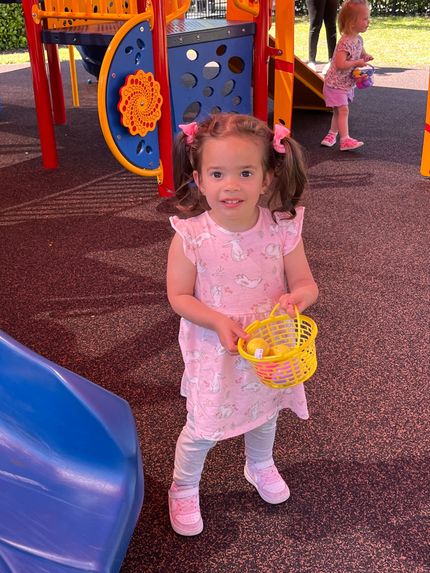 A little girl is holding a basket of easter eggs in a playground.