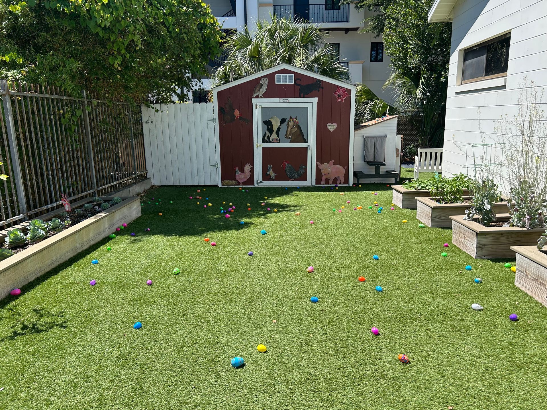 There are many easter eggs in the grass in front of a barn.