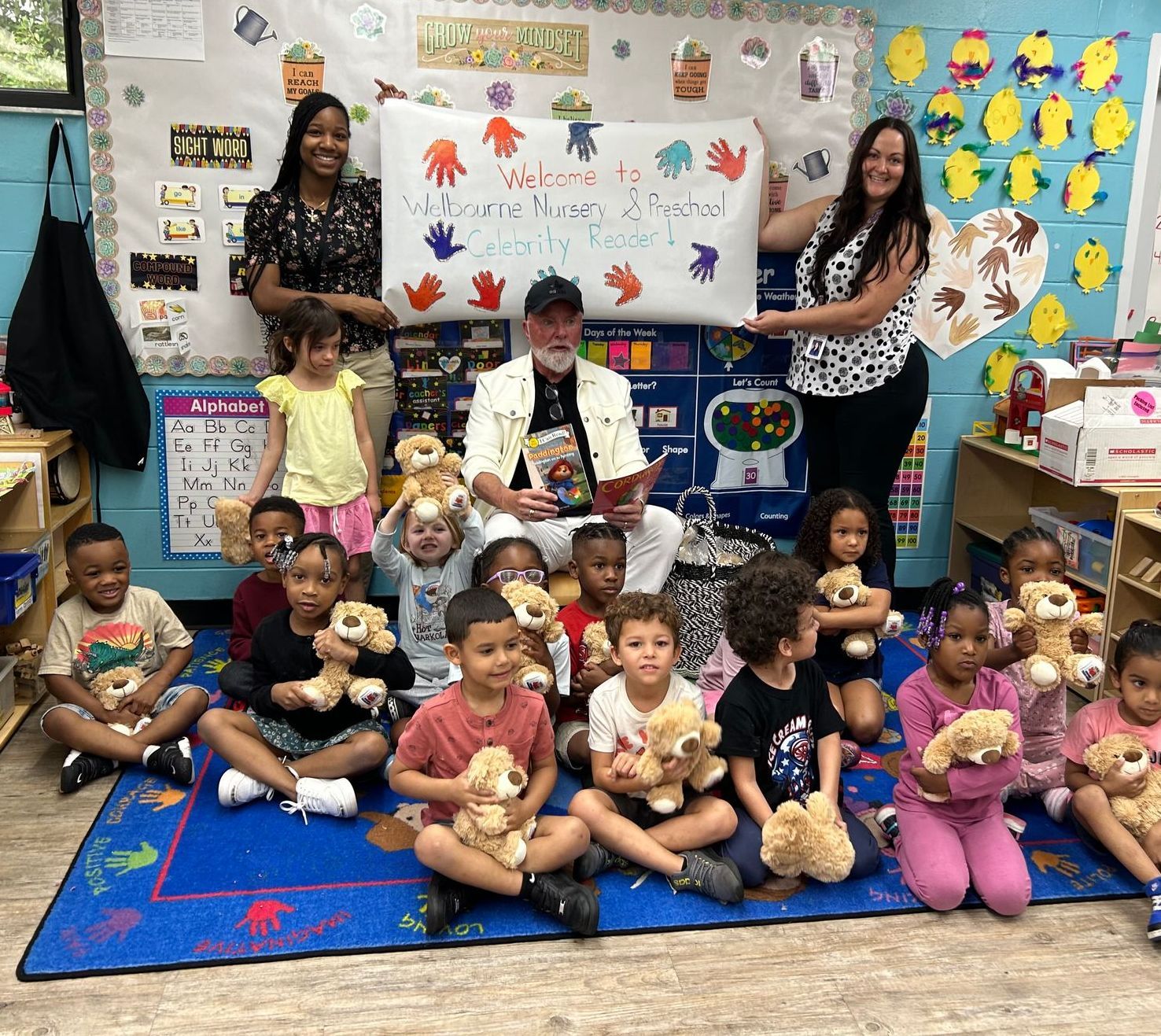 A group of children are sitting on the floor in a classroom holding teddy bears.