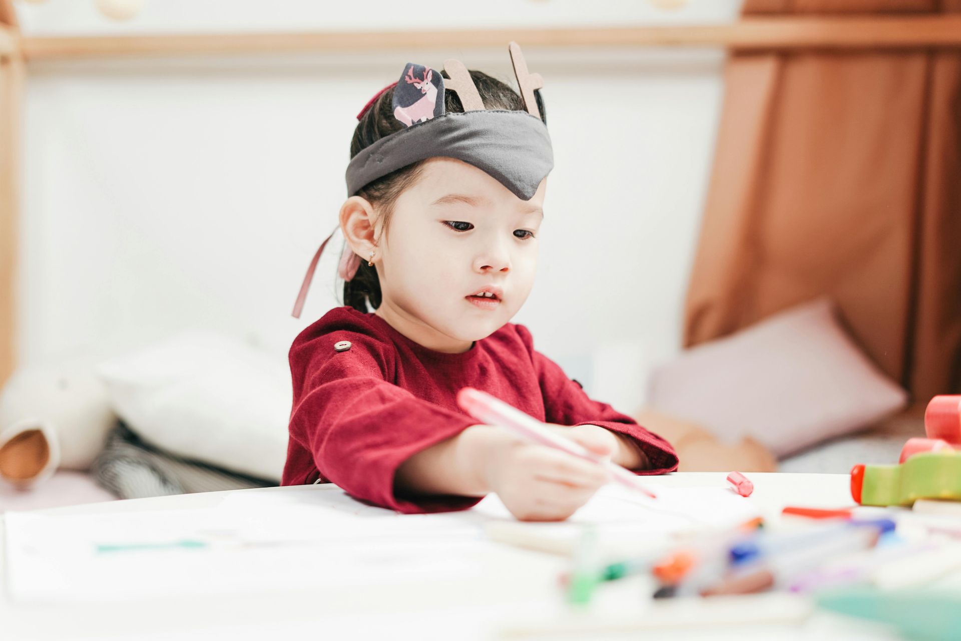 A little girl is sitting at a table drawing with markers.