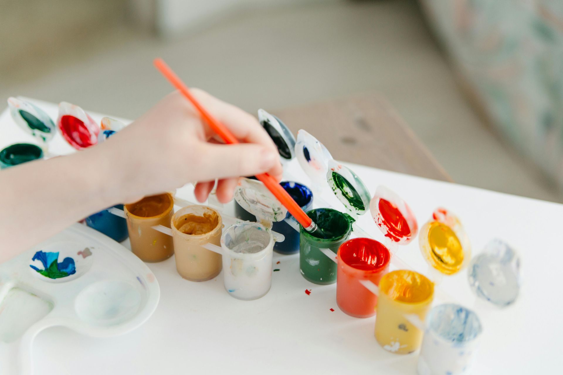 A child is painting with a brush on a white table.