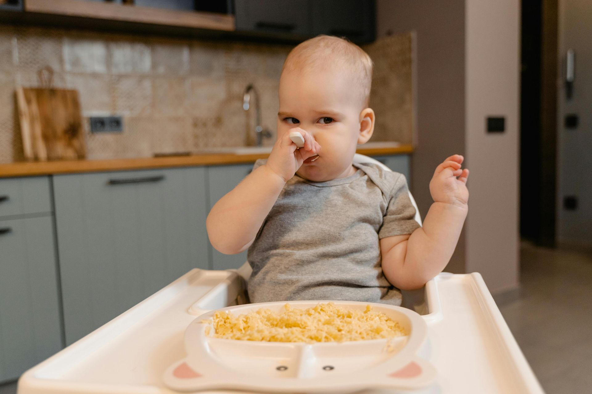 A baby is sitting in a high chair eating food from a plate.