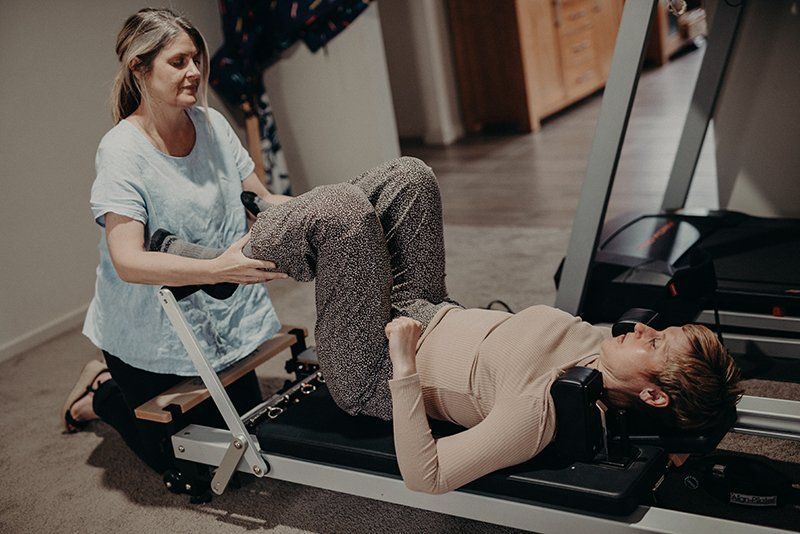 A woman is helping a woman do exercises on a pilates machine.