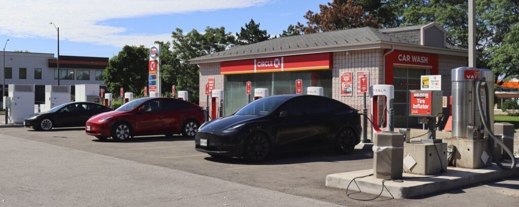 A row of cars are parked in front of a gas station.