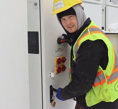 A man wearing a hard hat and safety vest is working on an electrical box