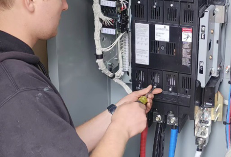 A man is working on an electrical box with a screwdriver