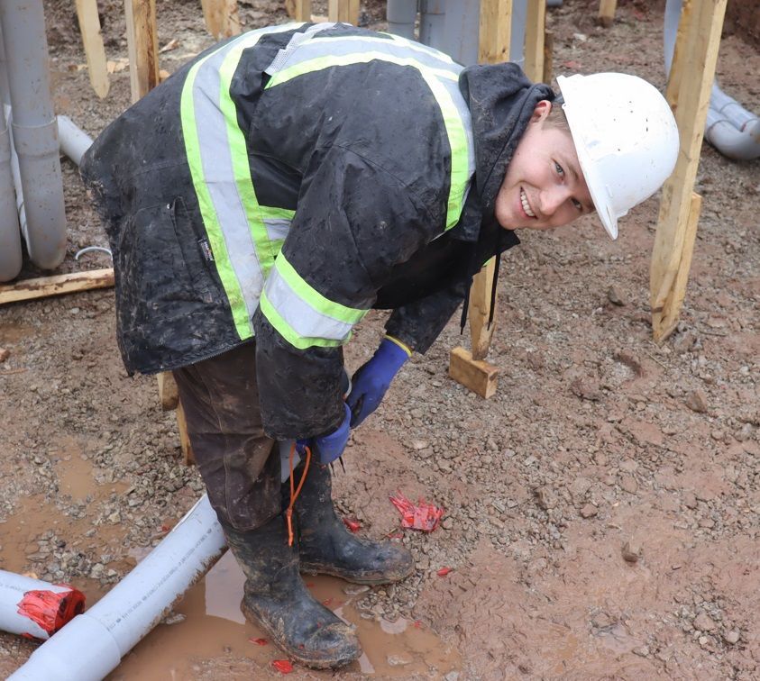 A man wearing a hard hat is bending over in the mud