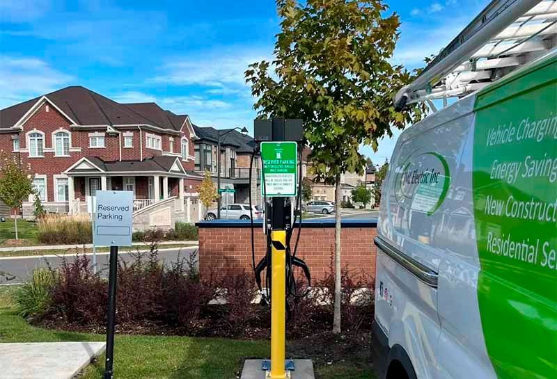 A green van is parked next to a charging station in front of a house.