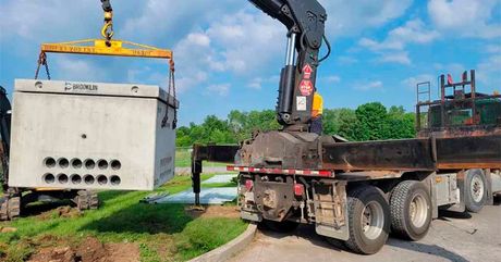 A large concrete box is being lifted by a crane on top of a dump truck.