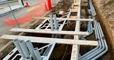 A bunch of pipes are laying in the dirt in a trench.