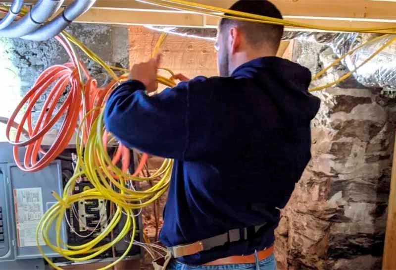 A man is working on electrical wires in a basement