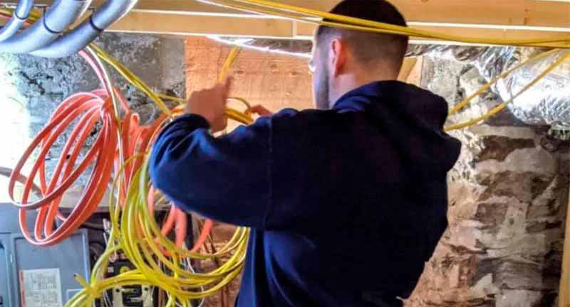 A man is working on electrical wires in a basement.