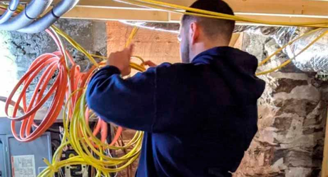 A man is working on electrical wires in a basement.