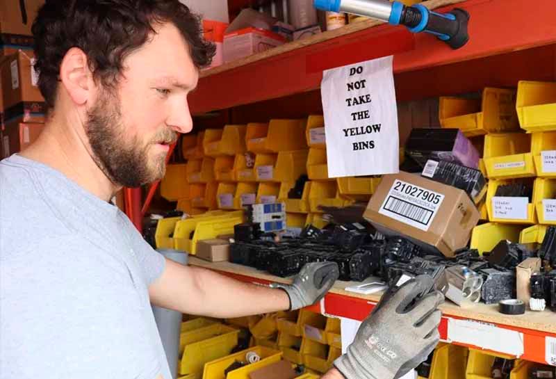 A man wearing gloves is standing in front of a shelf full of yellow bins.