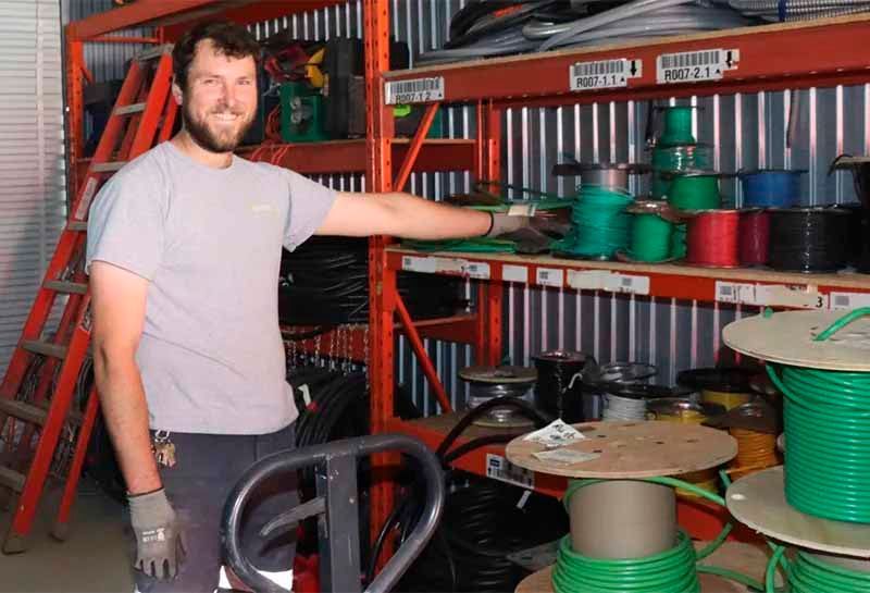 A man is standing in front of a shelf full of spools of wire.