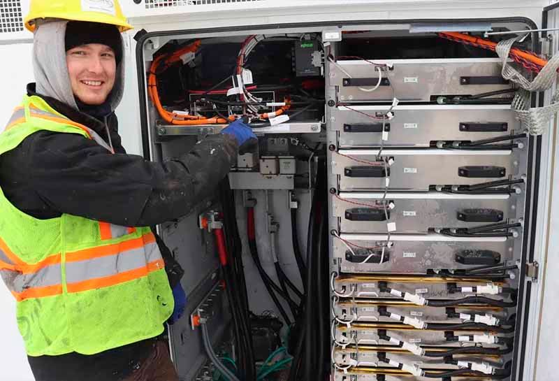 A man wearing a hard hat and safety vest is working on an electrical box.