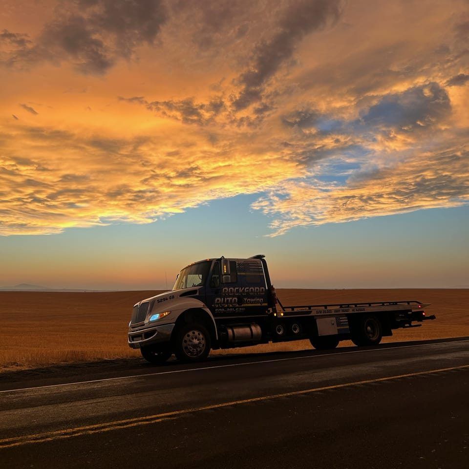 A tow truck is parked on the side of the road at sunset. | Rockford Auto Inc
