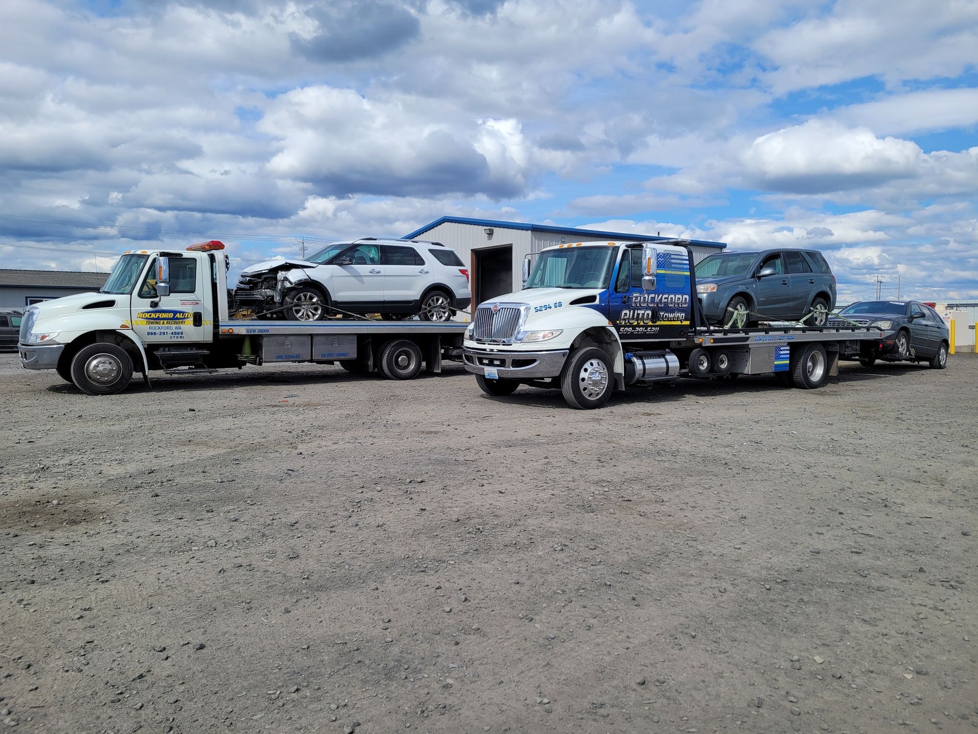 Two tow trucks are carrying cars in a gravel lot. | Rockford Auto Inc