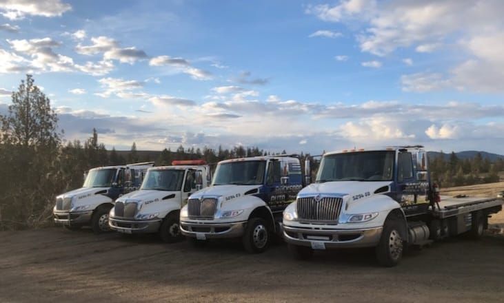 Two tow trucks are carrying cars in a gravel lot. | Rockford Auto Inc