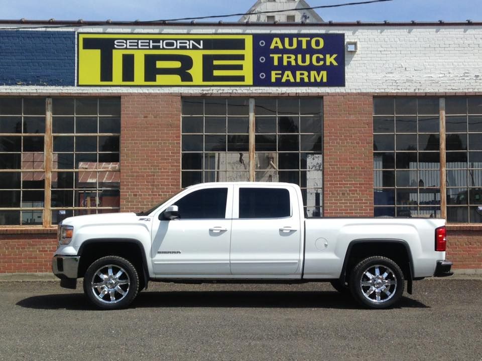 A white truck is parked in front of a beehorn tire auto truck farm