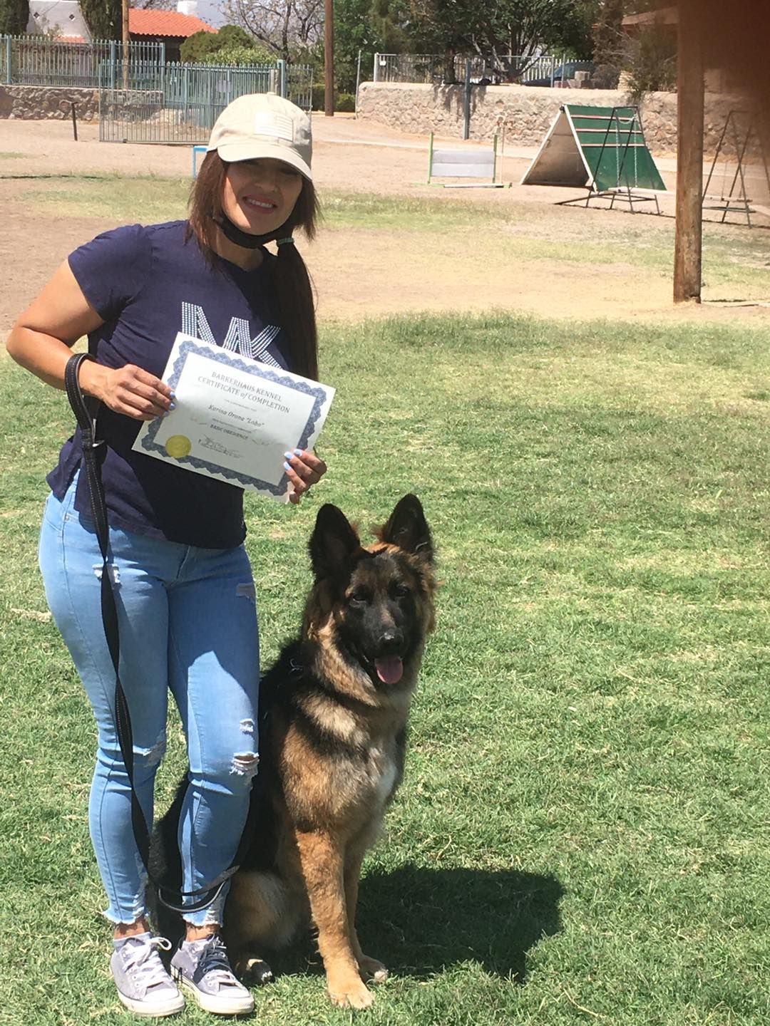 Woman with German Shepherd, holding a certificate, posing outdoors.
