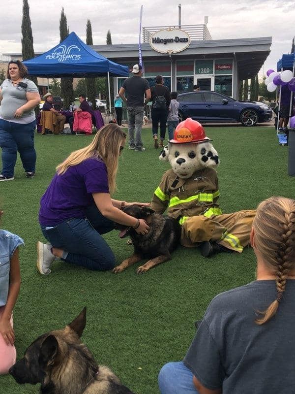 Woman pets dog next to firefighter mascot, in outdoor park setting.