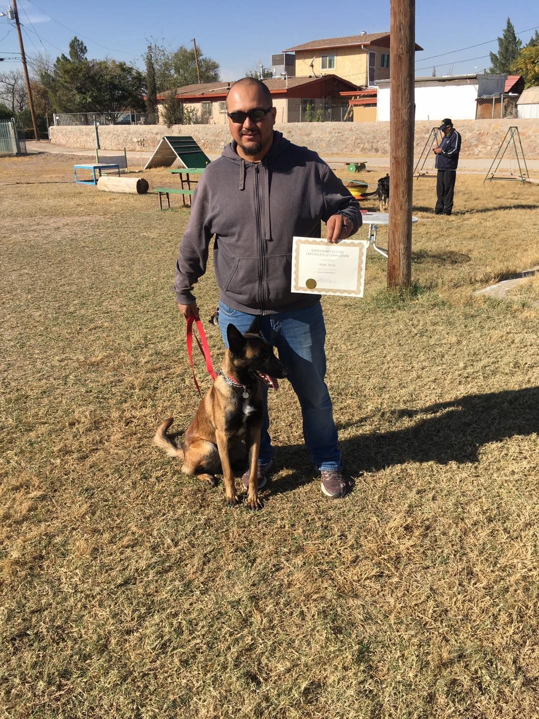 Man with certificate stands next to trained dog in park setting.