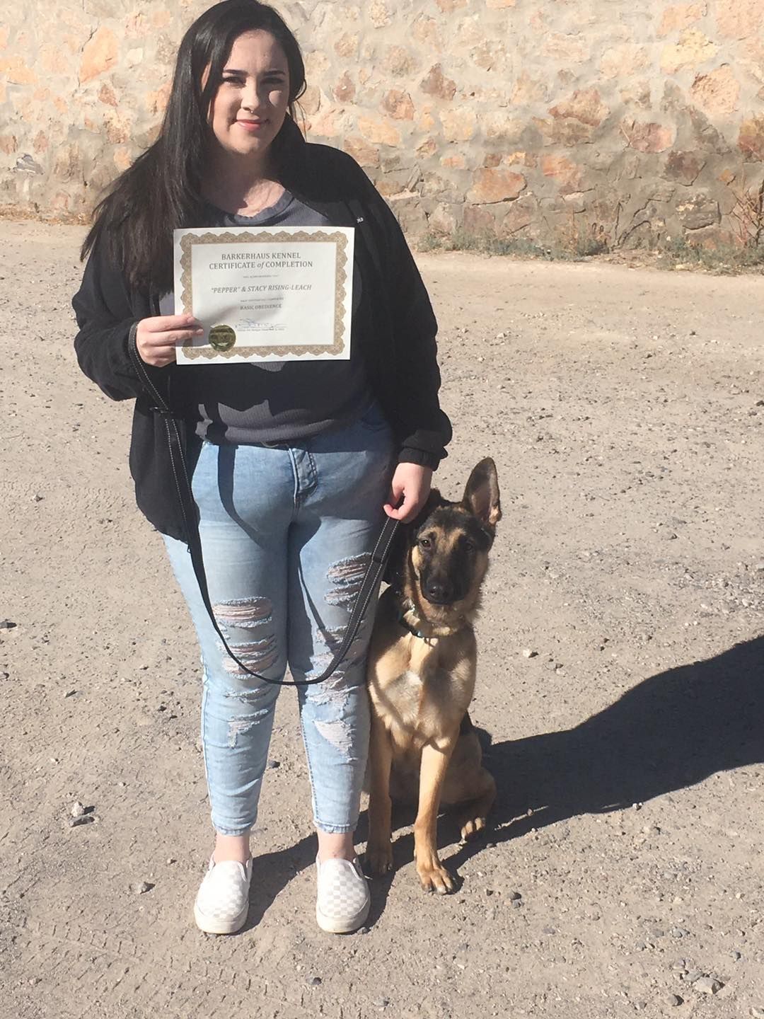 Woman in jeans and black jacket with German Shepherd; holding certificate.