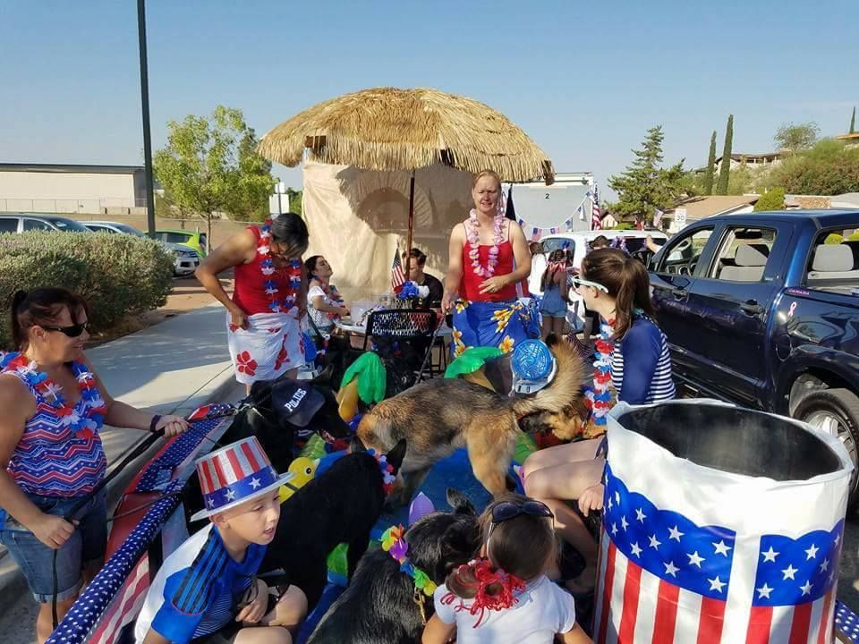 People and dogs on a float, decorated with patriotic themes, under a tiki-style structure.