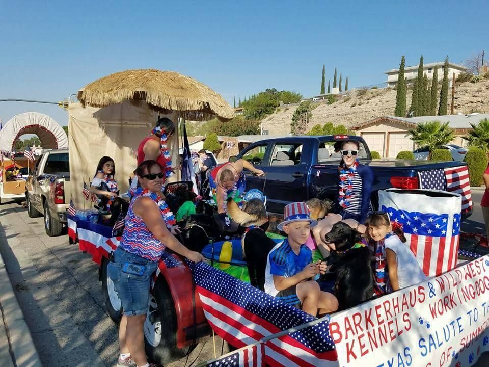 Parade float decorated in red, white, and blue with people, dogs, and American flags.