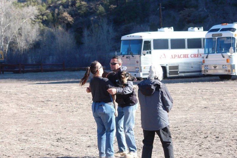 People hugging outdoors near parked buses labeled 