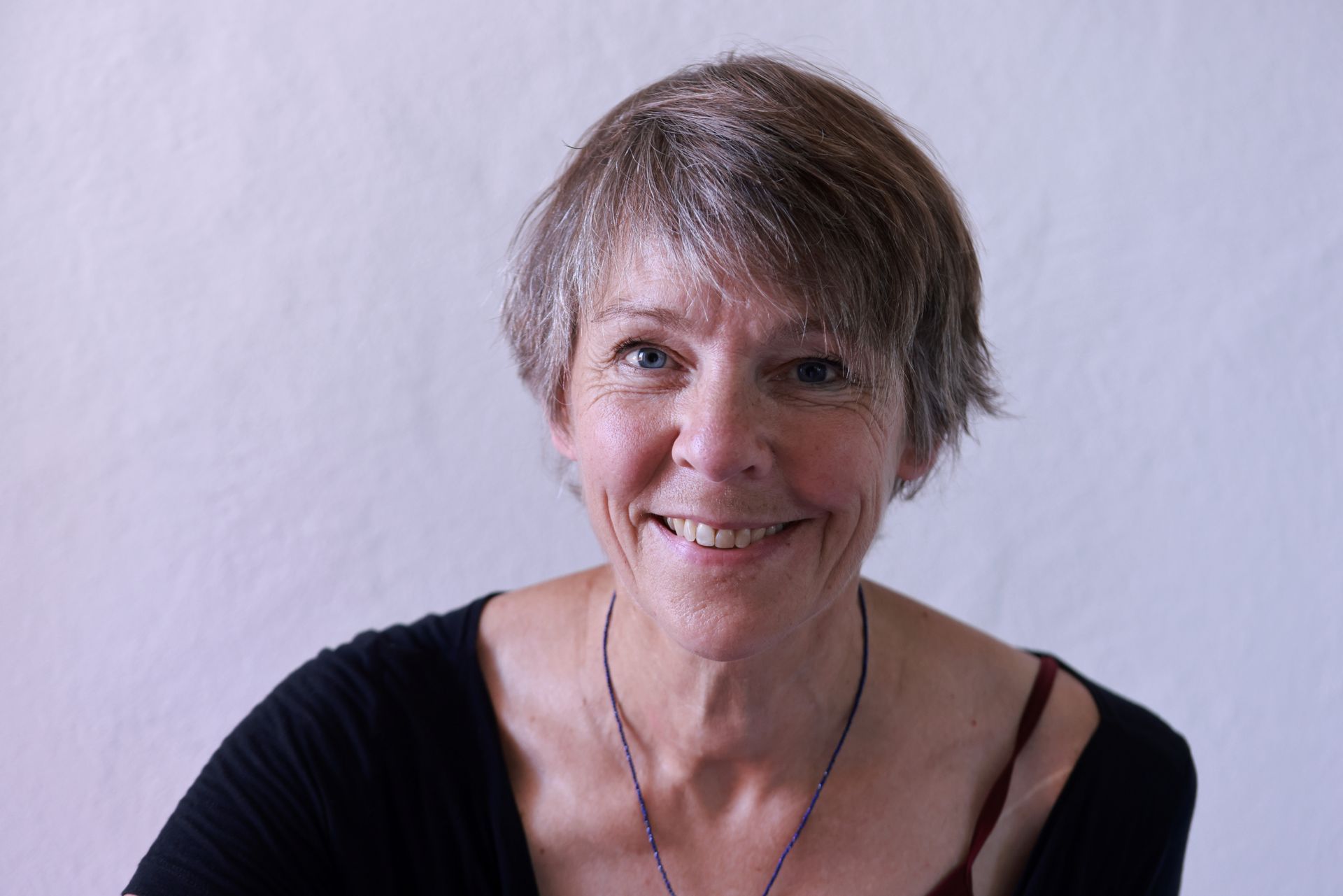 Eine Frau in schwarzer Jacke und lila Rollkragenpullover lächelt in die Kamera