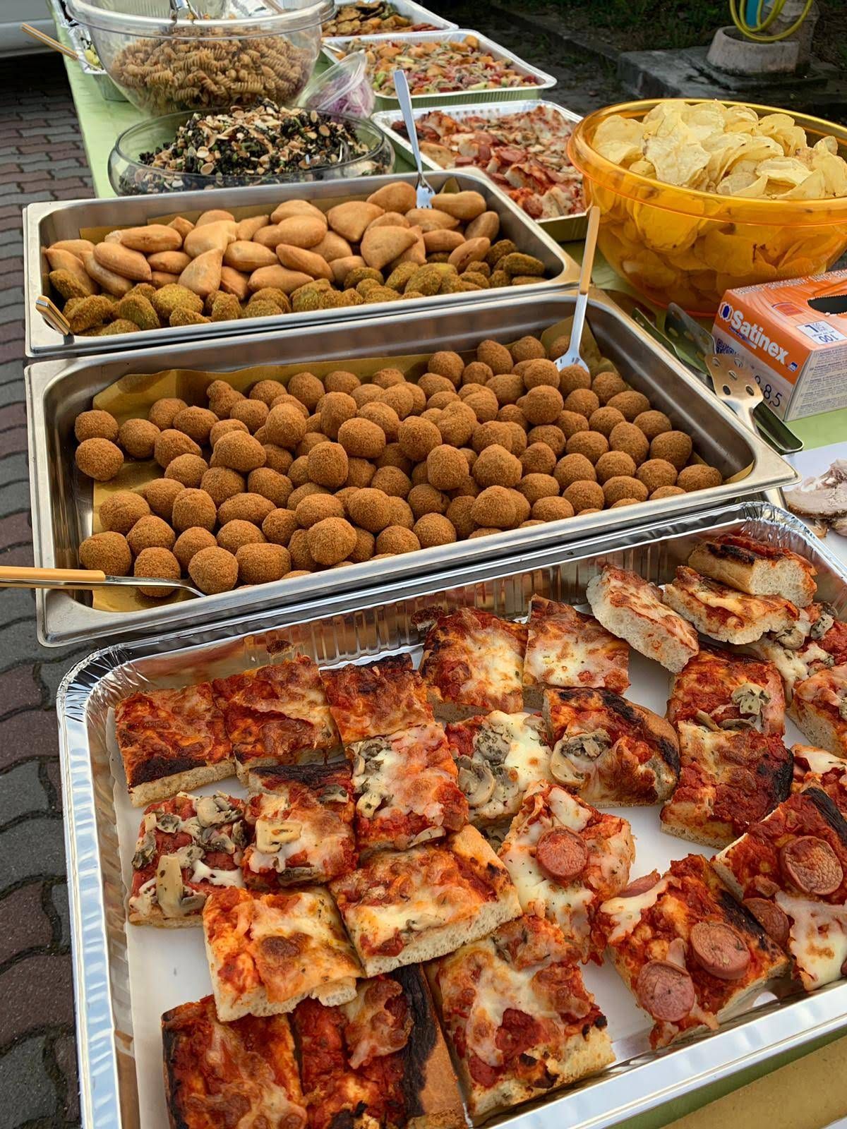 Tavolo da buffet all'aperto con vassoi di snack fritti, polpette e fette di pizza avvolte nella carta