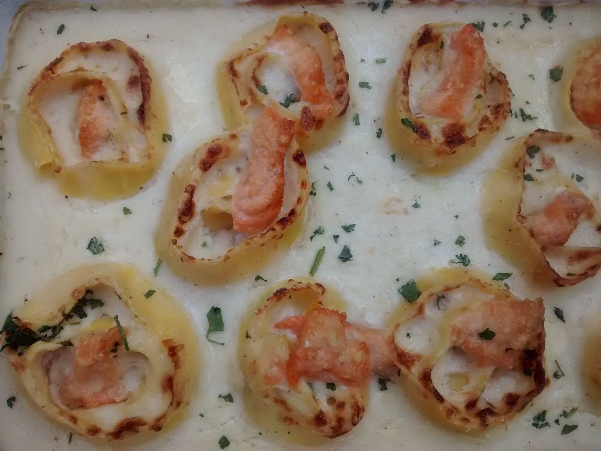 Gamberi al forno in salsa cremosa, guarniti con erbe aromatiche e disposti su un piatto bianco.