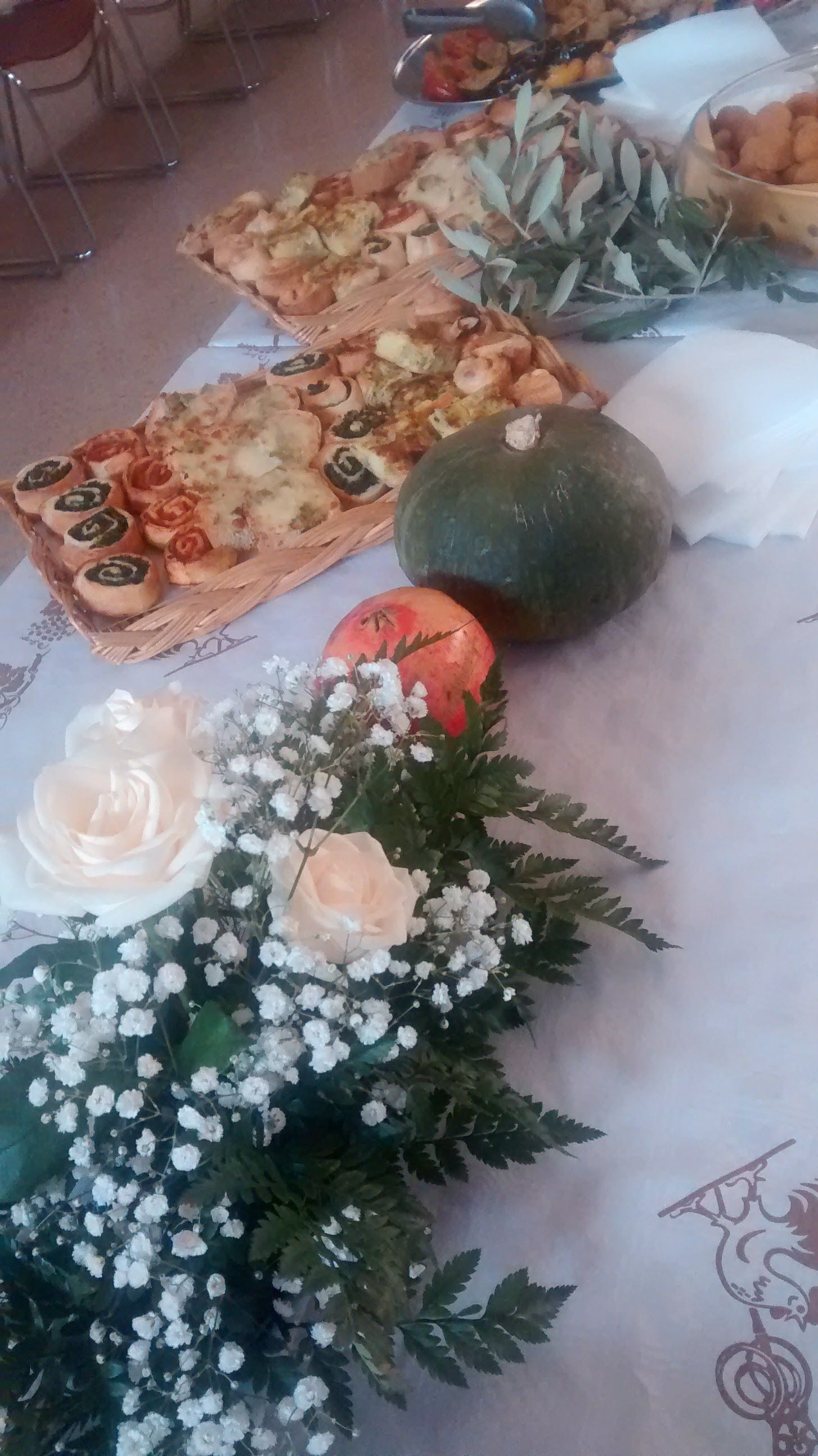 Pizze assortite, un melone e composizioni floreali bianche su un tavolo decorato.