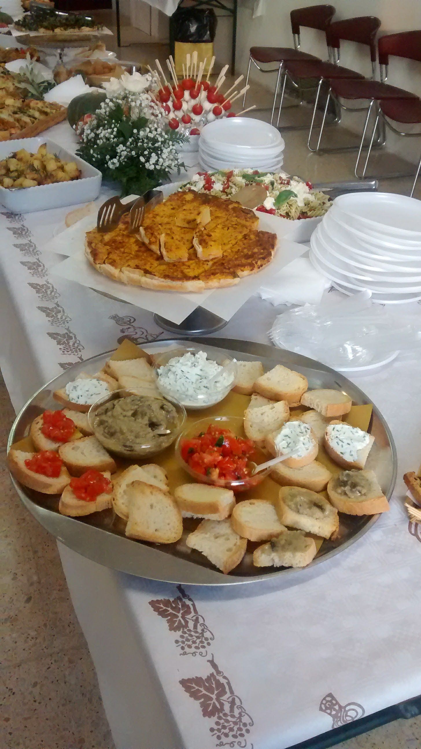Tavolo da buffet con antipasti assortiti, insalate e pane su una tovaglia bianca in una sala per banchetti.